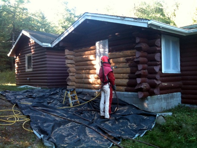 Tarps set below a person glass blasting a wood home.